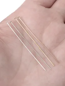 Detailed view of four multi-colored metallic T-pins for DIY jewelry making on palm