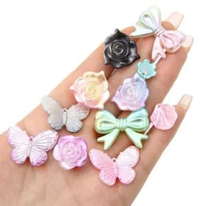 Various iridescent ABS pearl beads in rose and butterfly shapes shown on hand for scale