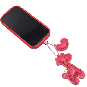 Dettaglio di ciondoli in pelle rosa a forma di cuore e giraffa su una custodia rossa.