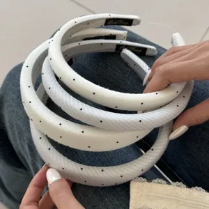 Detail von gepolsterten weißen Haarreifen mit schwarzen Punkten in den Händen.