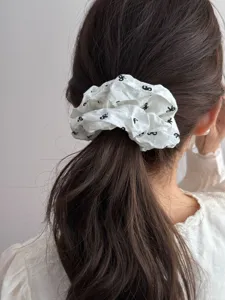 Close-up view of a white vintage fabric scrunchie with black bow patterns on a ponytail