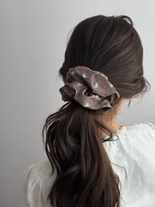 Detailed view of a retro brown fabric scrunchie with blue bow patterns on a ponytail