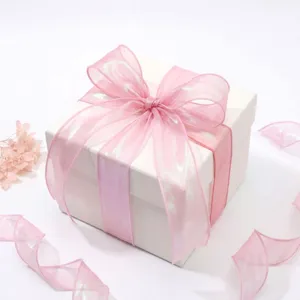 Ruban de gaze queue de poisson rose irisé noué sur une boîte cadeau blanche élégante.
