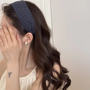 Vue détaillée d'un serre-tête large à carreaux bleus sur de longs cheveux ondulés.