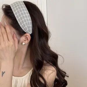 Gros plan d'un bandeau large à carreaux gris porté par un mannequin aux cheveux ondulés.