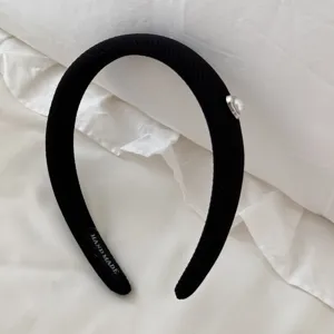 Close-up of a black ribbed headband featuring an elegant pearl heart detail on white fabric