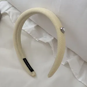 Close-up of cream textured padded headband with a heart-shaped pearl charm accent.