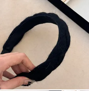 Detailopname van een zwarte wollen gevlochten haarband met dikke gebreide textuur.