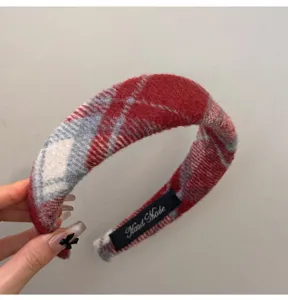Detailed macro shot of a cozy red plaid wool headband featuring a Hand Made label