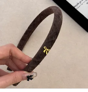 Primo piano di un cerchietto stretto in velluto marrone con un piccolo fiocco dorato.