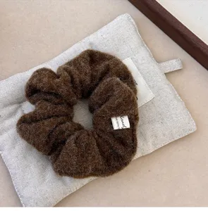 Close-up of a brown plush felt scrunchie with soft fuzzy texture and brand label detail.