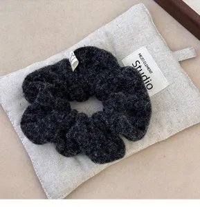 Detailed view of a dark grey textured wool scrunchie placed on a neutral linen pouch.