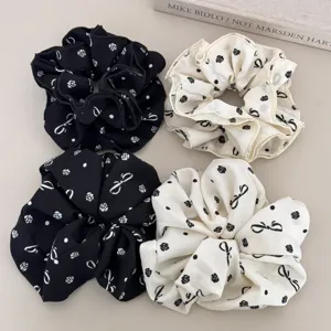 Close-up of floral and bow print scrunchies in elegant black and white silk fabric.
