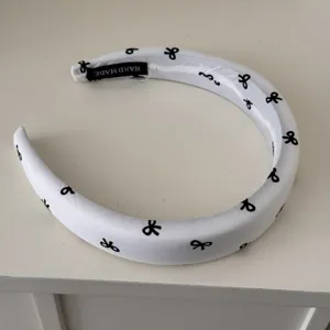Detailed macro view of a white padded headband with black bow print and handmade tag