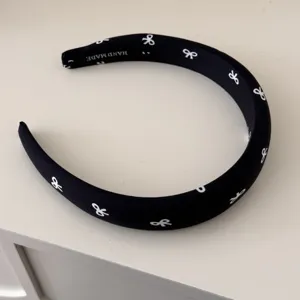 Detailed view of black fabric headband featuring white bow patterns and handmade tag