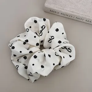 Detail shot of a chic white scrunchie with elegant black rose and bow prints.