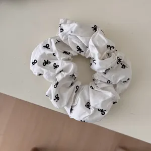 Close-up of a white fabric scrunchie featuring a minimalist black bow print design