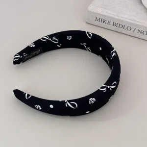 Close-up of black headband with white bow and rose patterns on a minimalist background.