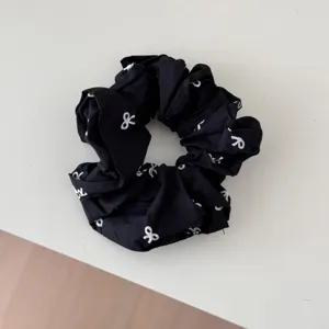 Close-up detail of a black fabric scrunchie with white bow-knot pattern