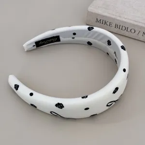 Detailed view of a white padded headband featuring elegant black rose and bow prints