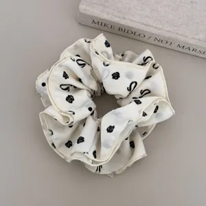 Detail view of a white scrunchie featuring elegant black floral and bow patterns on fabric