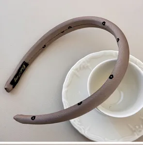 Close-up of taupe sponge headband featuring delicate black flower patterns and texture