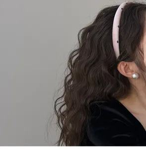 Close-up view of a pink padded headband with small black flowers and pearl earring.