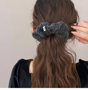 Close-up detail of a model with long wavy hair wearing a grey plush fuzzy hair scrunchie