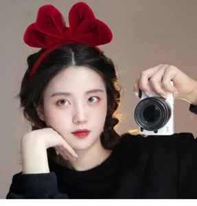 Aziatisch model met een stijlvolle rode fluwelen strik haarband, houdt een witte camera vast.