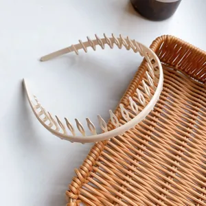 A close-up detail view of a beige minimalist long-tooth plastic headband on a rattan tray