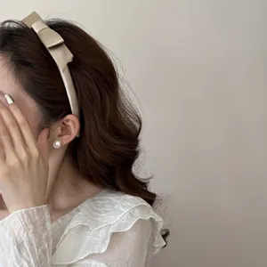 Detailansicht eines eleganten beigefarbenen Haarreifens mit Satinschleife an einem Model.