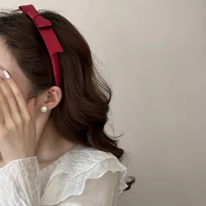 Nahaufnahme der Seitenansicht eines eleganten bordeauxroten Satin-Bogen-Stirnbands für Damen