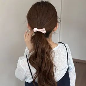Dettaglio di un elegante fiocco di seta rosa per capelli su una coda di cavallo mossa castana