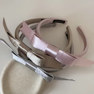 Detailansicht von drei eleganten Satin-Haarreifen mit Schleifen in Rosa, Gold und Silber