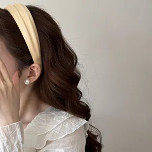 Detail view of a French high-top wide fabric headband in beige on wavy brown hair.