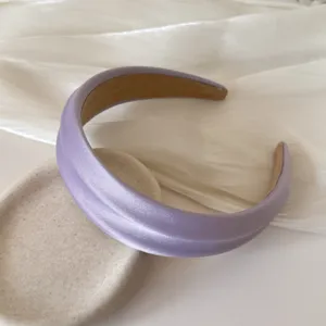 Detail view of lavender satin padded headband with subtle sheen on textured background