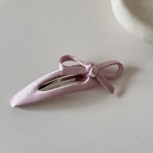 Primo piano di un fermaglio per capelli rosa con fiocco in raso e texture in seta.