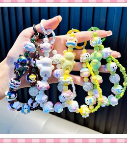 Hand holding colorful beaded cartoon bear phone charms and keychains in macro detail
