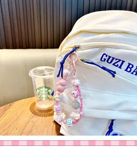 Detailed shot of a pink beaded bear bag charm attached to a white backpack zipper