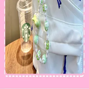 Detailweergave van een groen-witte kralenhanger met vogelornament aan een witte tas