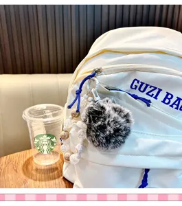 Detalle de un llavero con pompón esponjoso en blanco y negro y cuentas en una mochila
