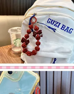 Detail van een rode kralenhanger met strikken aan een witte rugzak en een telefoonhoesje.