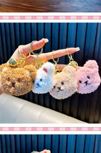 Four colorful plush teddy bear keychains with gold bells held in hand as bag charms