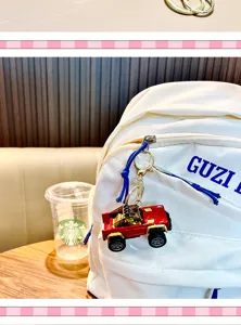 Close-up detail of a red toy pickup truck keychain charm hanging from a white backpack zipper