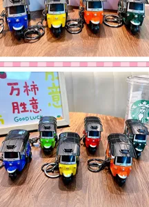 Colorful pull-back tuk-tuk tricycle toy keychains in various vibrant colors on a wooden table