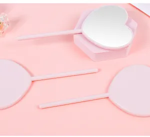 Close-up of pink heart-shaped lollipop style handheld mirrors on pink background