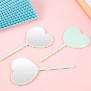 Cute heart-shaped hand mirror with lollipop handle in mint green on pink background