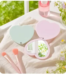 Detailed view of the heart-shaped rotating double-sided travel makeup mirror on fabric.
