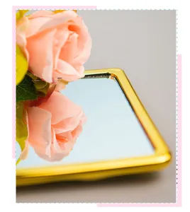 Close-up of gold-plated handheld makeup mirror with rose reflection and metallic finish