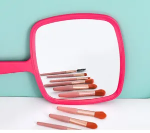 Gedetailleerd zicht op een grote roze handspiegel met reflectie van make-up kwasten